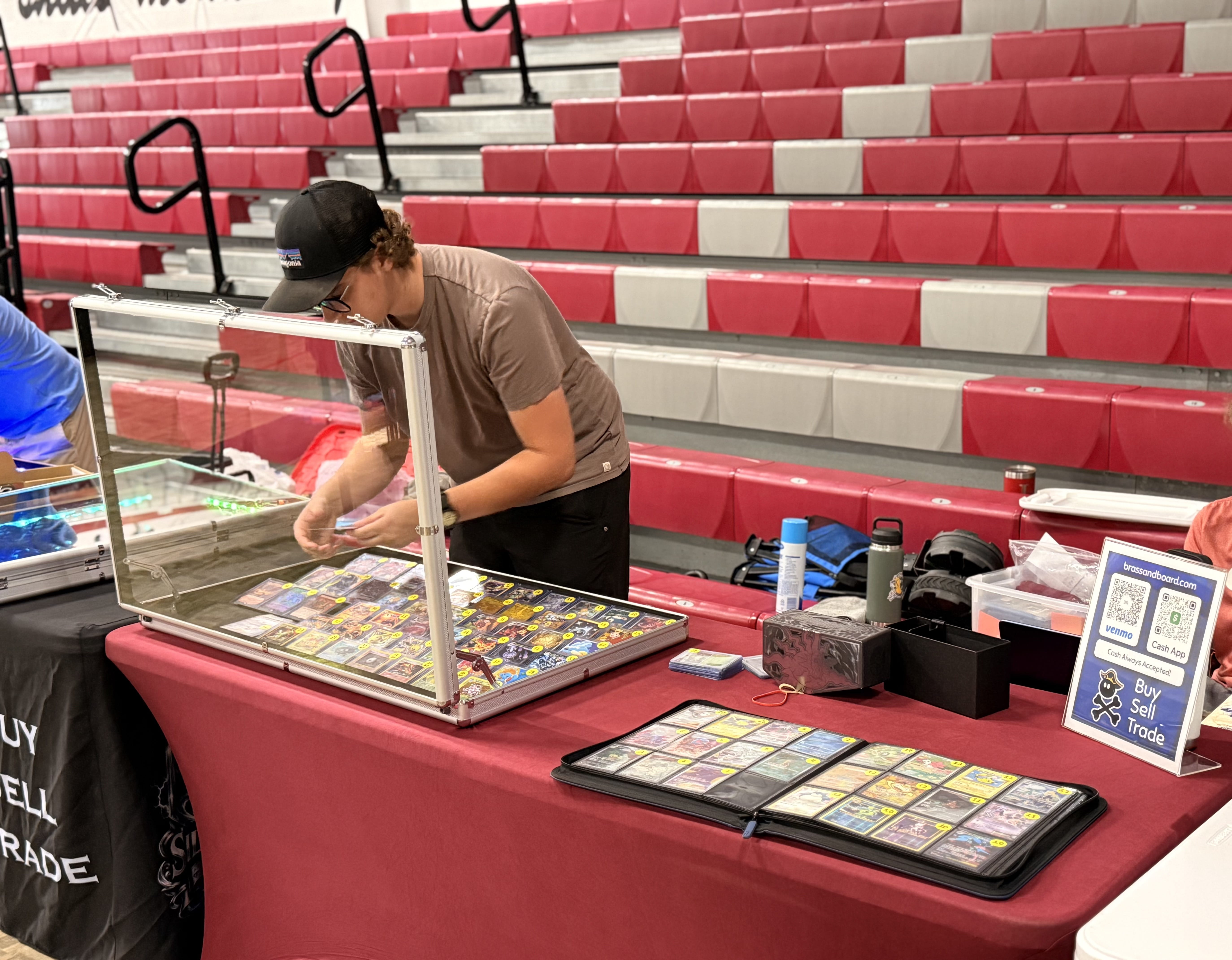 Beckett setting up his display case at a Nashville card show, with a binder of cards and the Brass & Board sign on the table